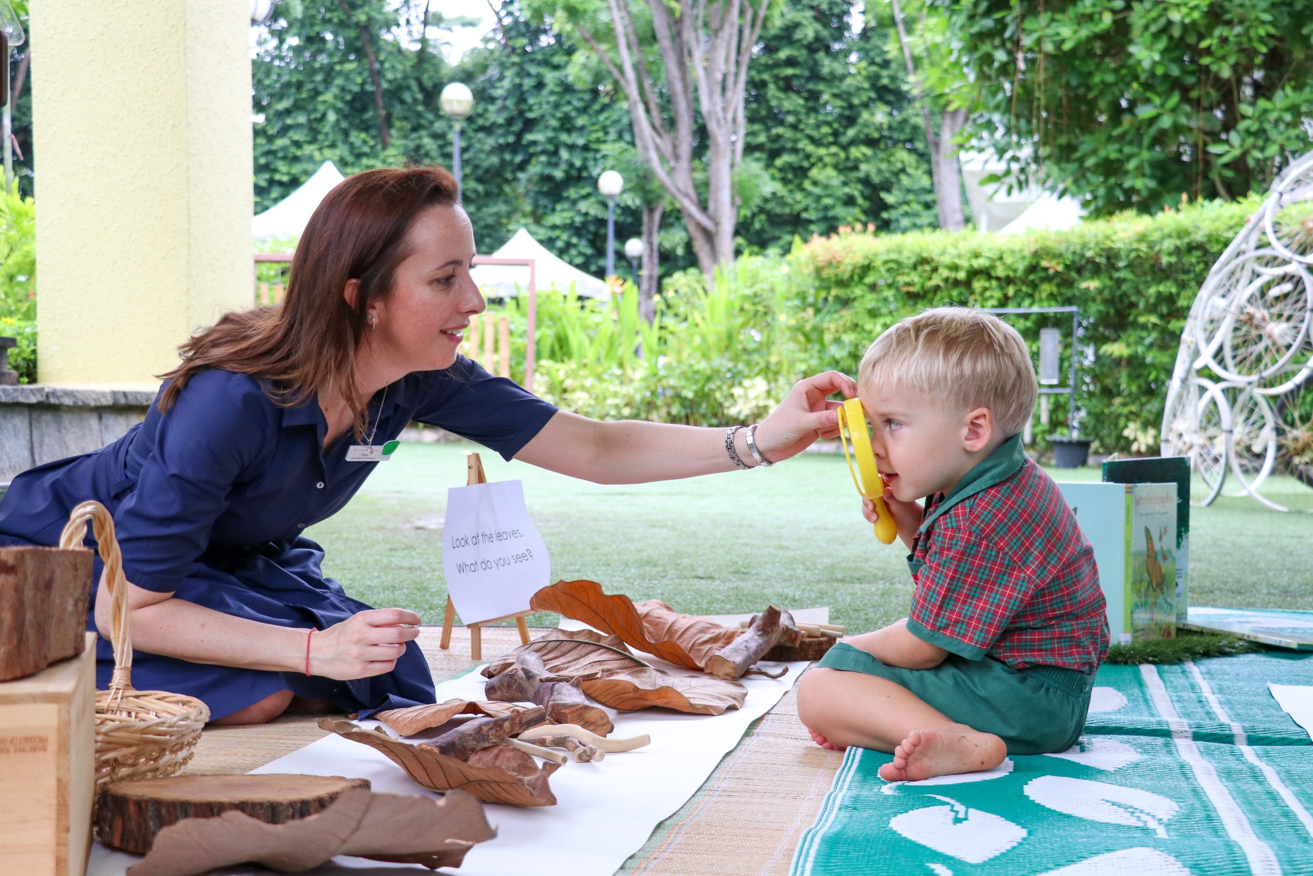 EtonHouse Riyadh - An adult guiding a child outdoors at a sensory-rich play area, surrounded by natural garden elements.